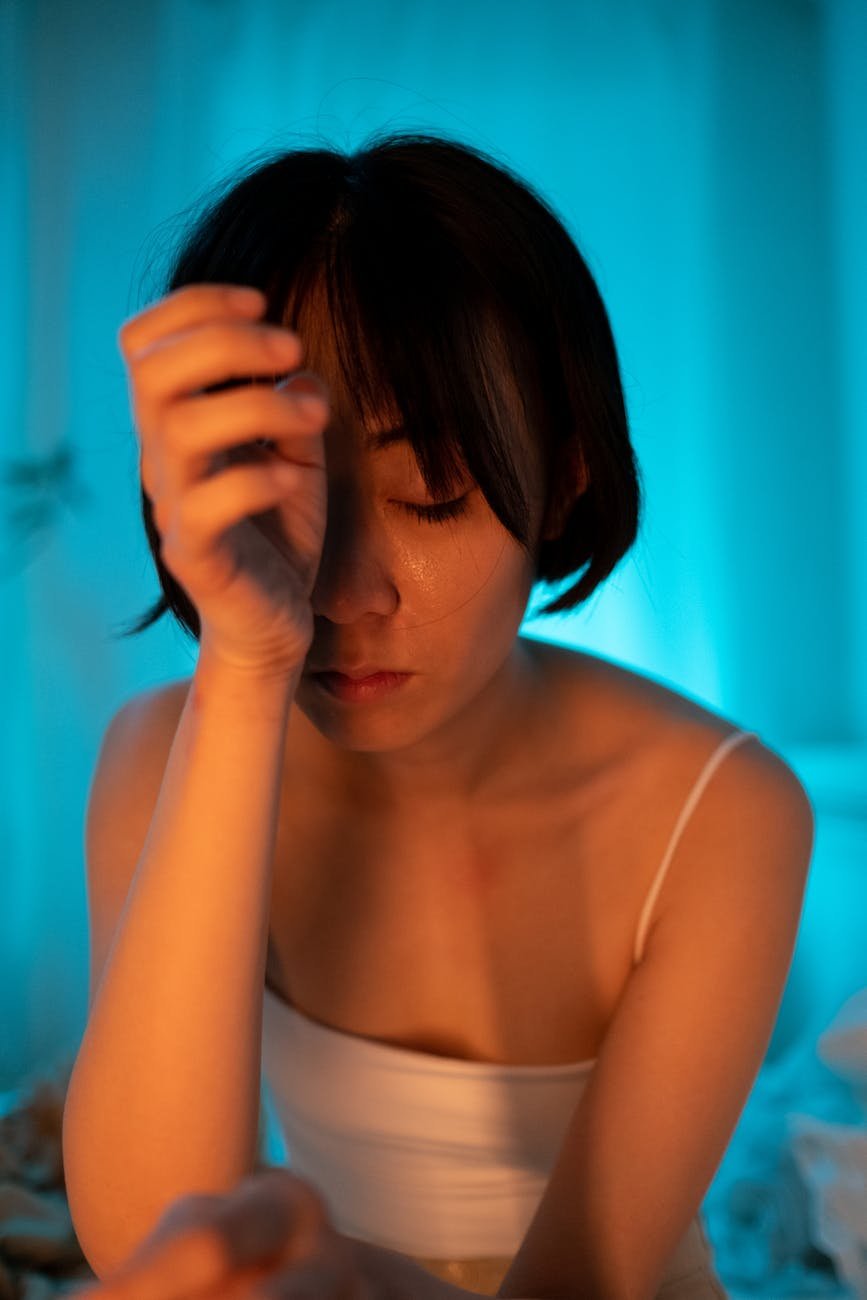 a short haired woman in white tank top with her hand on her face